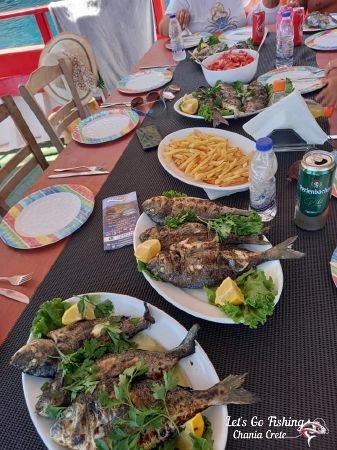 Full table with grilled fish and fires and Greek Salad. Fishing trips. Visit Greece. Crete LEt's Go fishing